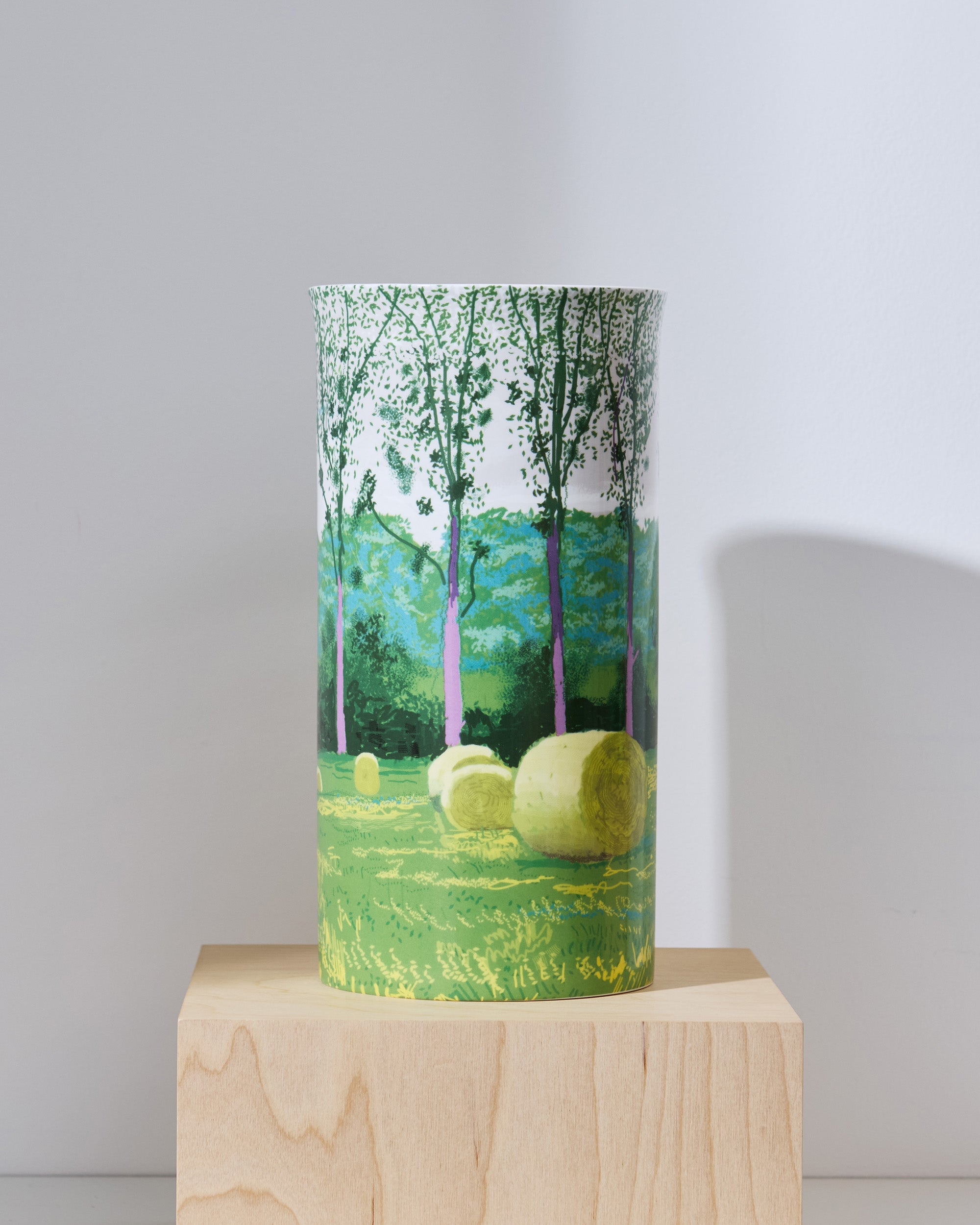 Tall cylindrical container with a forest design on a wooden block against a white background
