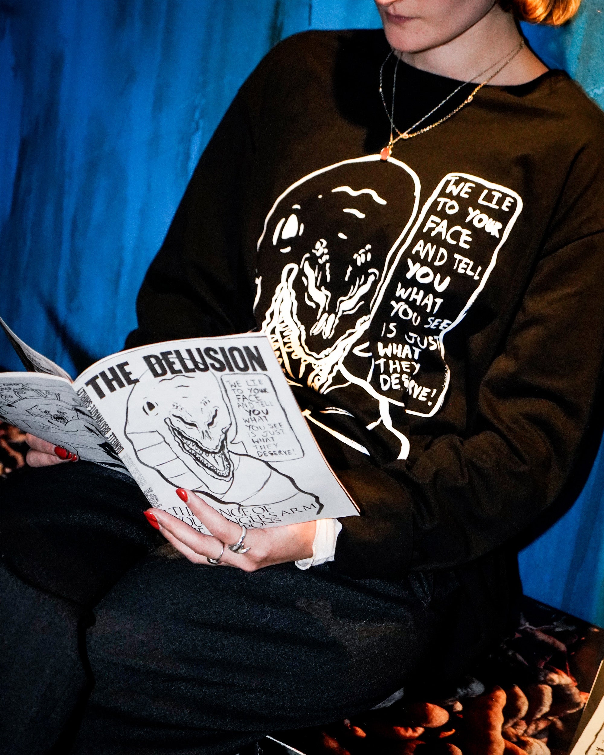 Person wearing a black sweatshirt with a graphic design and holding a book titled 'The Delusion'.