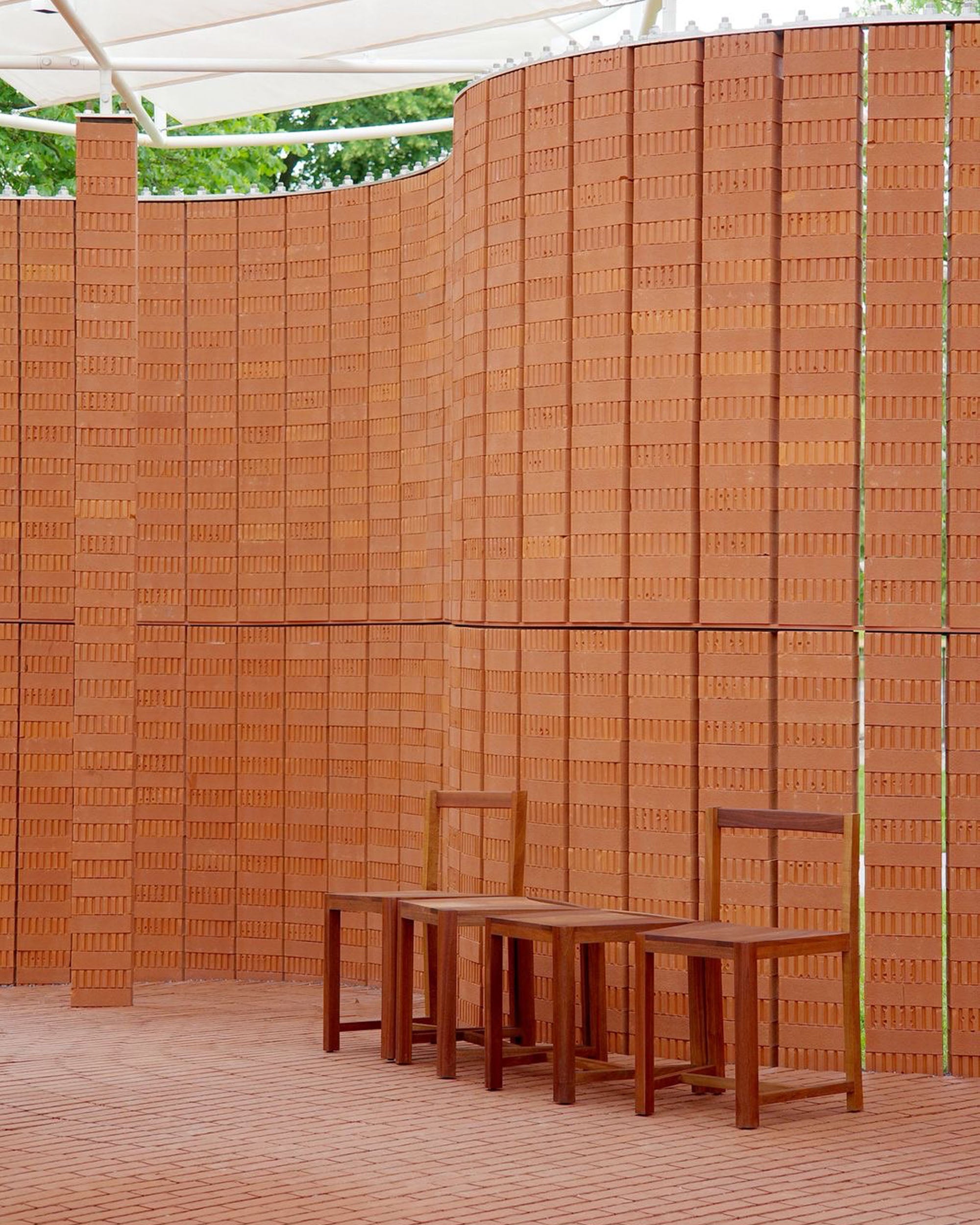 Wooden chairs and tables against a brick-patterned wall.